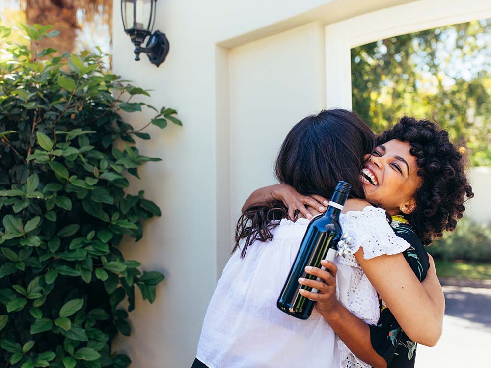 Woman greeting new homeowners with a bottle of wine.